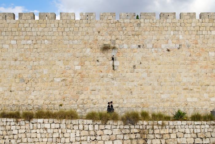 "Beyond a Temple" - a photo of two people walking along a high wall in Jerusalem.