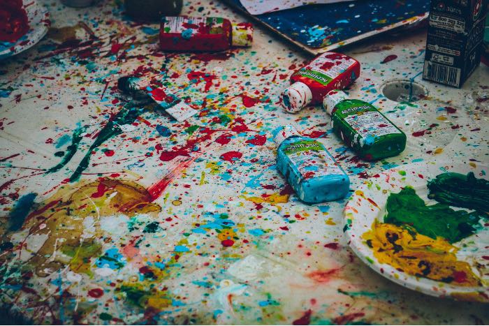 "Saintly Messy" - a photo of a paint-splattered surface, bottles of paint cast around