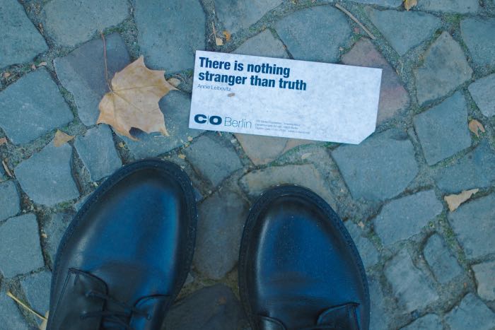 "How the political binary breaks our brains." - a photo from the perspective a person looking on the ground, their shoes visible, and a card in on the walk which reads "there is nothing stranger than truth."