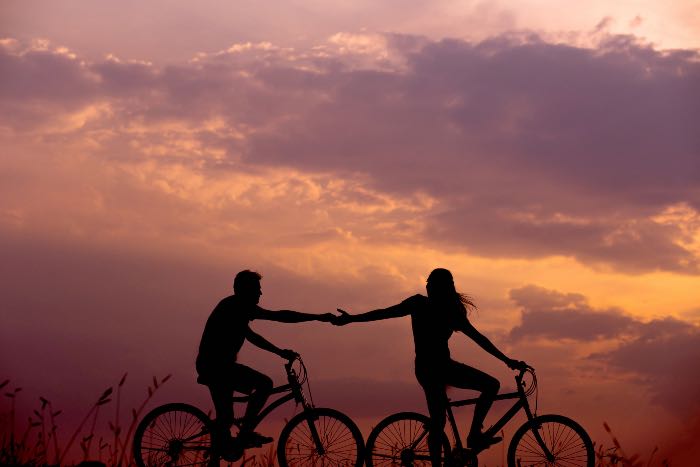 "Beloved" - a photo of two people reaching out and holding hands while riding bikes.