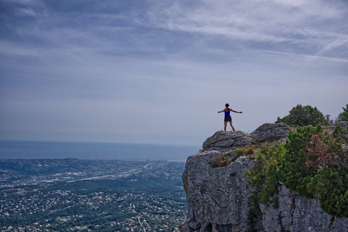 "Achievement" - a photo of a person by the edge of a cliff, arms spread out.