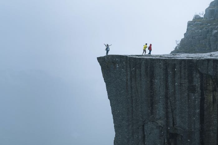 "confidence and grace" - a photo of people on a cliff: one by the edge, arms out, and two others walking away.