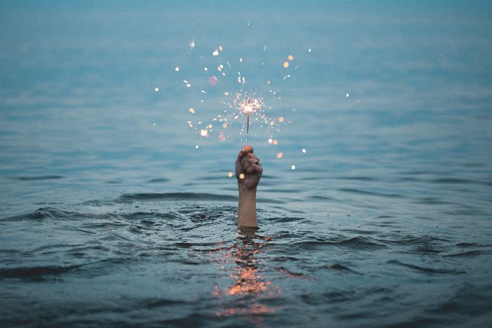 "still poor in spirit" - a photo of a hand, out from the water, holding a sparkler.