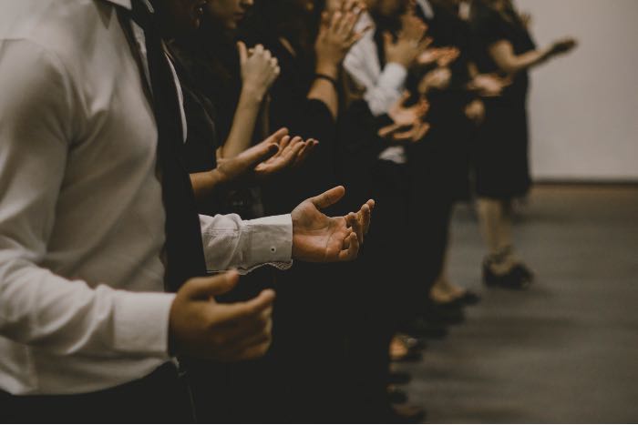 a photo of people, in a row, praying, hands open.