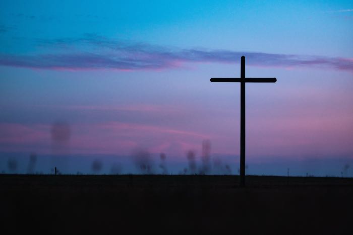 a photo of a cross in front of a dark, sunsetting or rising sky