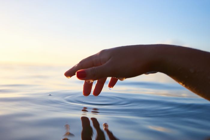 a photo of a hand over water, fingers, just touching, a circle ringing out