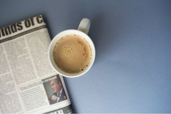a photo of a cup of coffee and a newspaper folded up