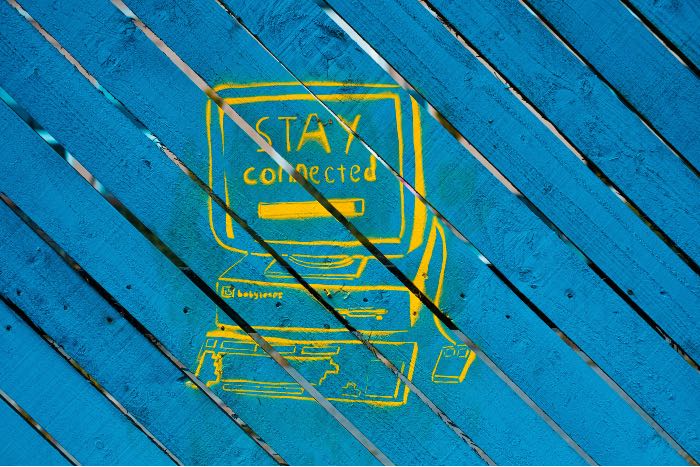 a close-up photo of a fence, painted blue, with a rough painting of a computer and on the screen it says "stay connected".