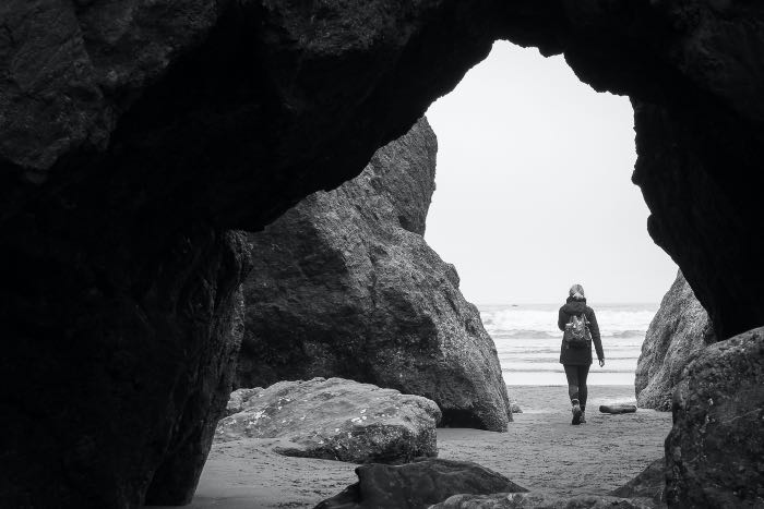 a person walking away from a cave by the beach