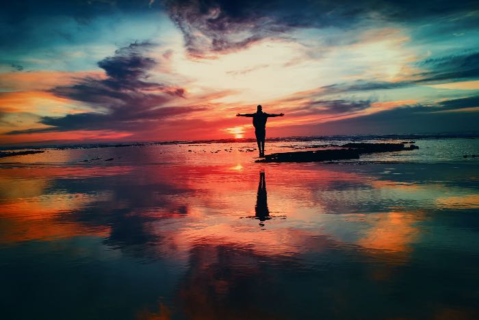 a photo of a person, arms wide, at sunset; the colors are radiant and extreme