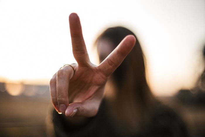 a photo of a person giving the peace sign, her hand is in focus, close to the camera