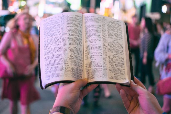 a photo of two hands holding up a Bible while on a city street with people passing by