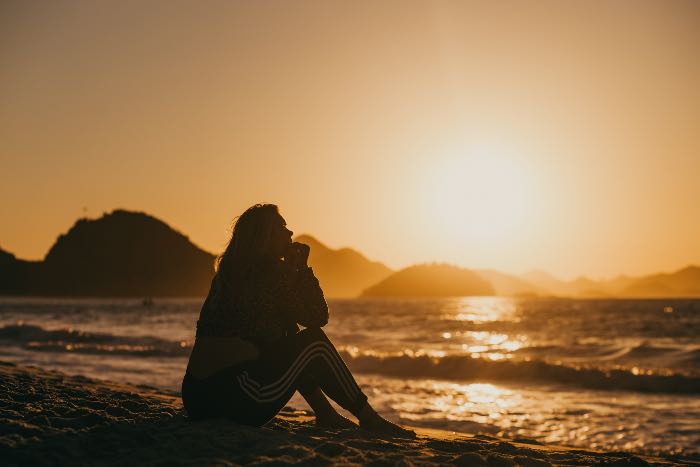a photo of a person sitting on the beach at sunrise