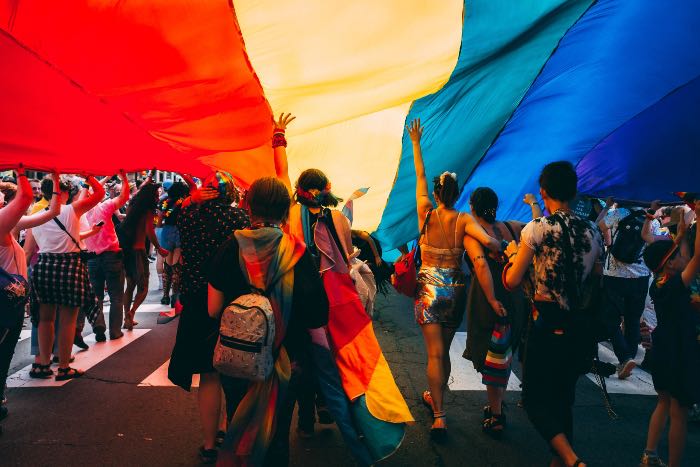 a photo of people celebrating Pride under a giant rainbow tarp