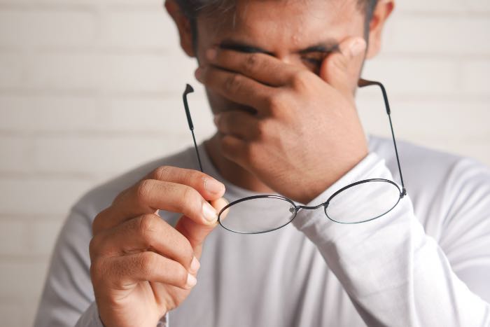 a photo a man, holding his glasses while rubbing his eyes.