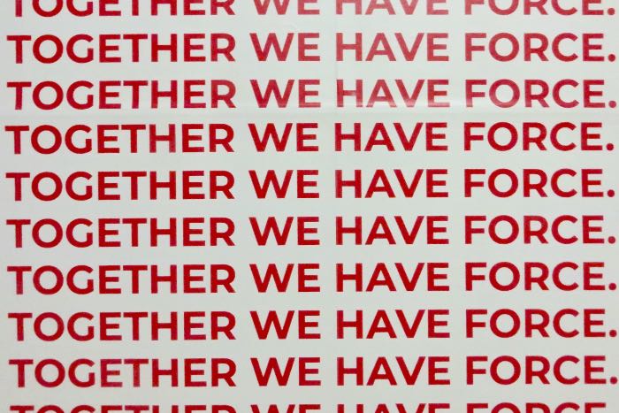 a photo of what appears to be a poster, white background with the same sentence repeated over and over in red: "Together we have force."