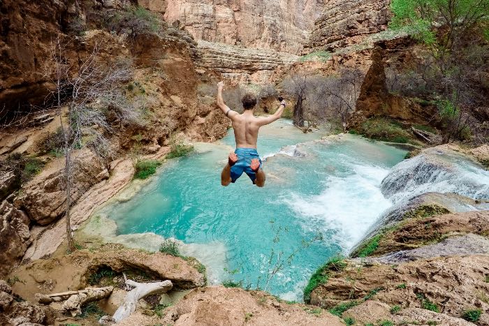 a person leaping from a cliff toward a pool of water