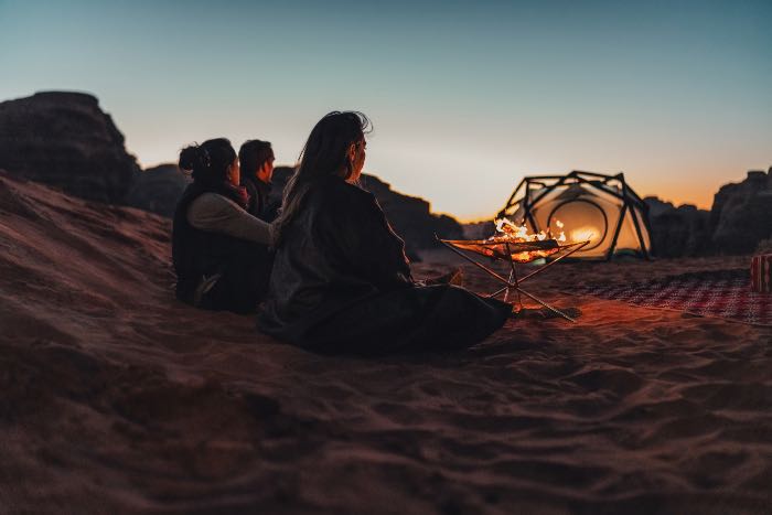a photo of three people sitting in sand near a tent