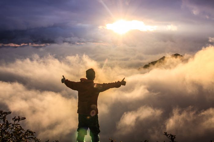 a photo of a person on the top of a mountain, arms out, among clouds