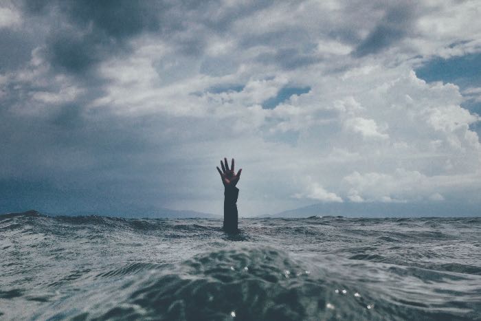 a photo of a hand reaching up out of open water, evoking the need for help