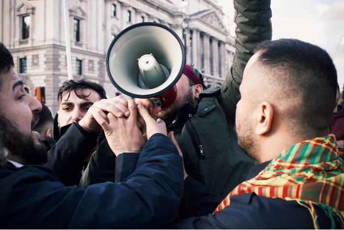 "Why "they started it" is the defense of the guilty" — a photo of protestors, one with a bullhorn, another appears to want to take it from him.