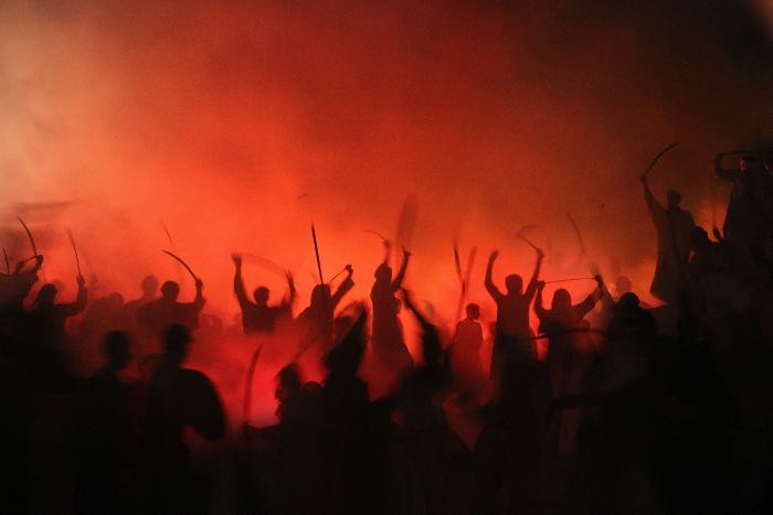 a photo in red, with shadows of people, arms raised, surrounded by menacing smoke