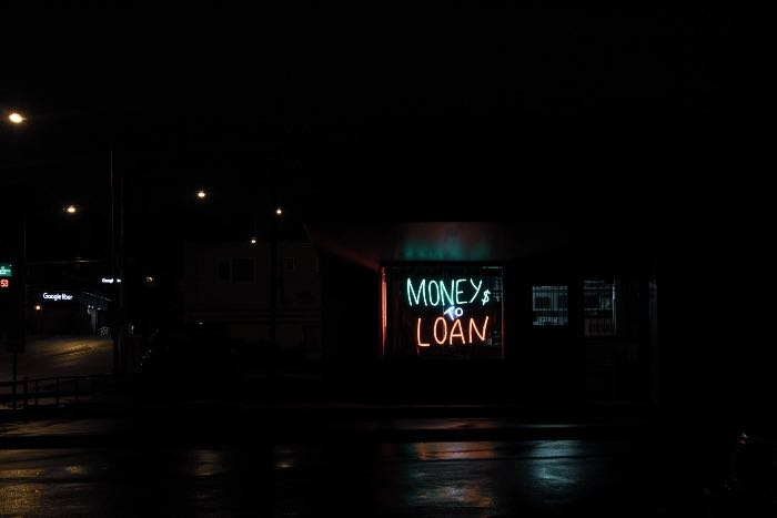 A photo of a dark city street, a neon sign in a shop front reads: "MONEY TO LOAN"