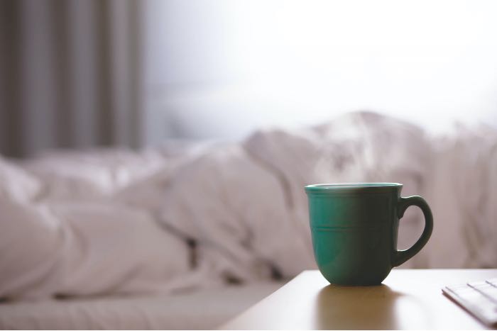 a photo of a green ceramic mug on a wooden desk next to a bed