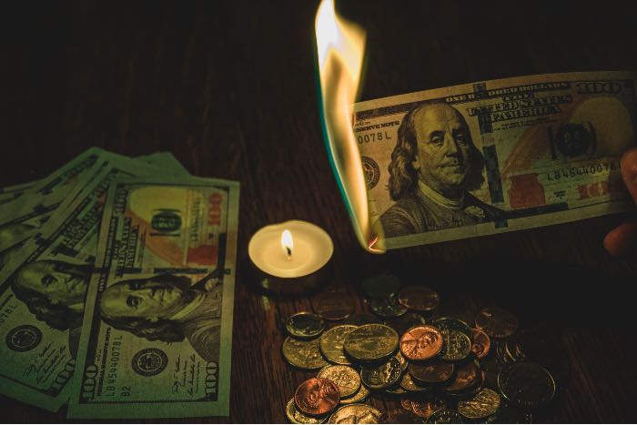 a photo of money on a table, a candle in the center, and a $20 bill lit on fire.