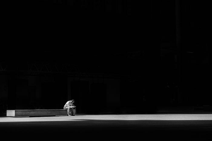 a photo of a person sitting on the bench in the dark—a strip of light crossing the floor