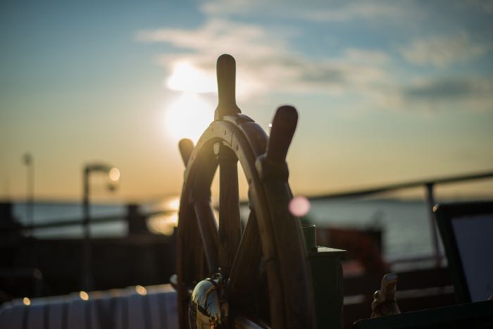 a photo of the wheel of a ship, the sun setting behind it
