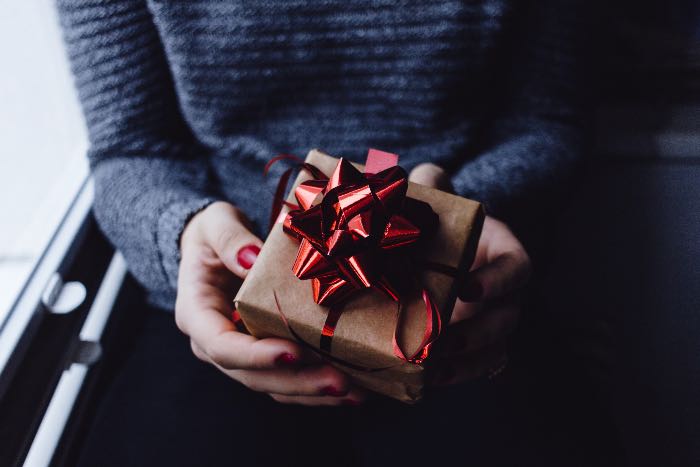 a photo of a person holding a gift wrapped in brown paper and a red bow