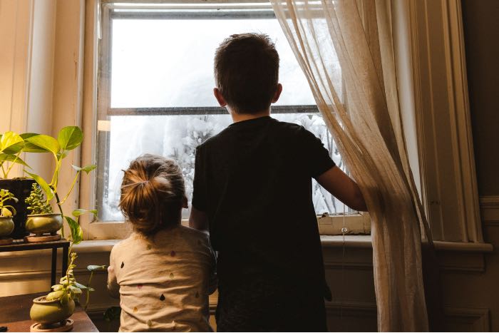 a photo of two kids looking out the window in their pajamas.