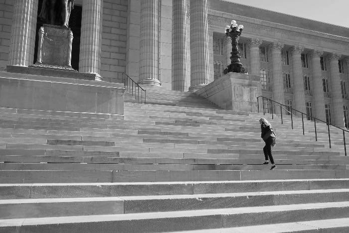 a photo of a person waling up the stairs to a big building