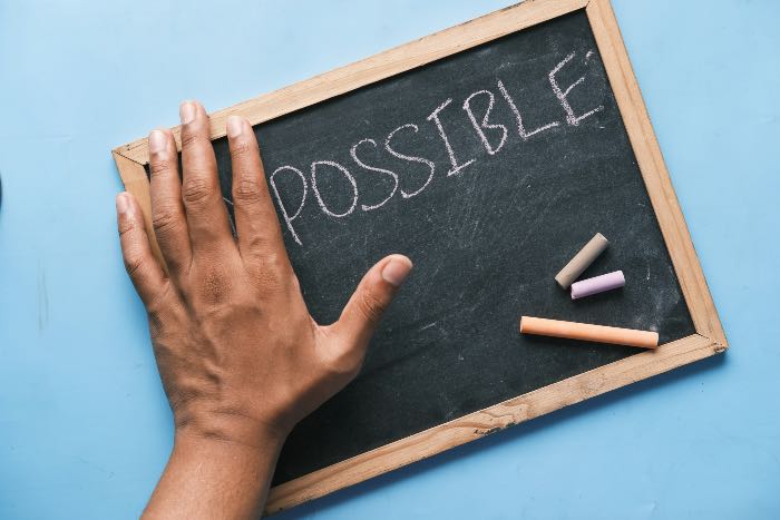 a photo of a chalkboard with a hand covering part of it, with the word "POSSIBLE" visible.