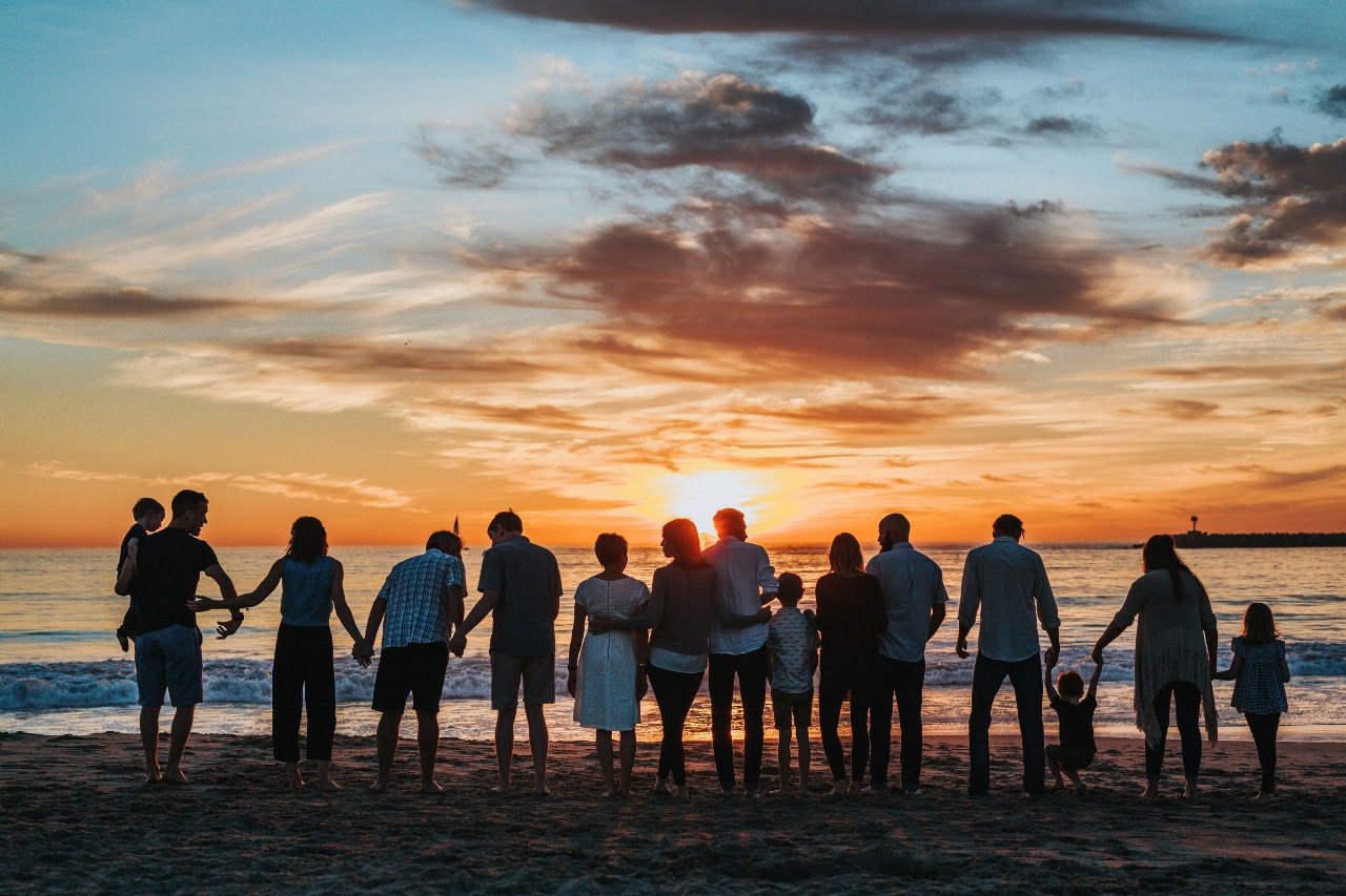 a photo of an assortment of people standing and watching the sunset on the beach