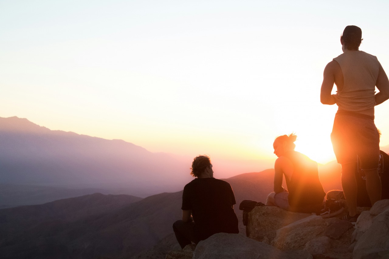 a photo of people talking on a mountaintop, sun setting behind them.