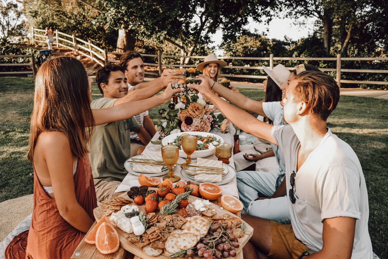 a photo of friends gathered around a table outside, clinking glasses