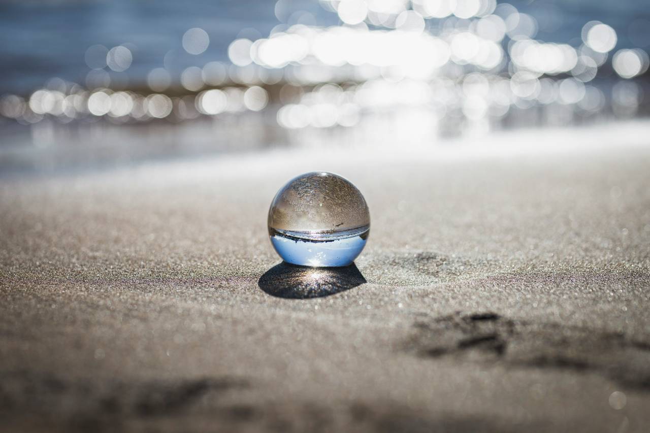 a photo of a glass ball on the beach, flipping the beach and sky in its reflection