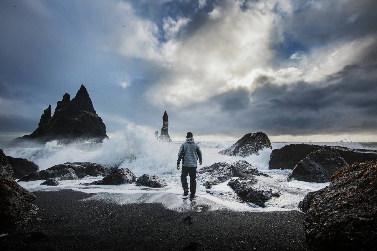 a photo of a person walking into the water, with waves cascading off of rocks
