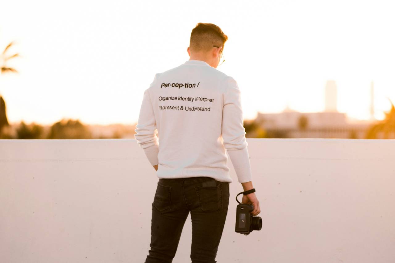 a person holding a camera. His shirt offers a definition of "perception"