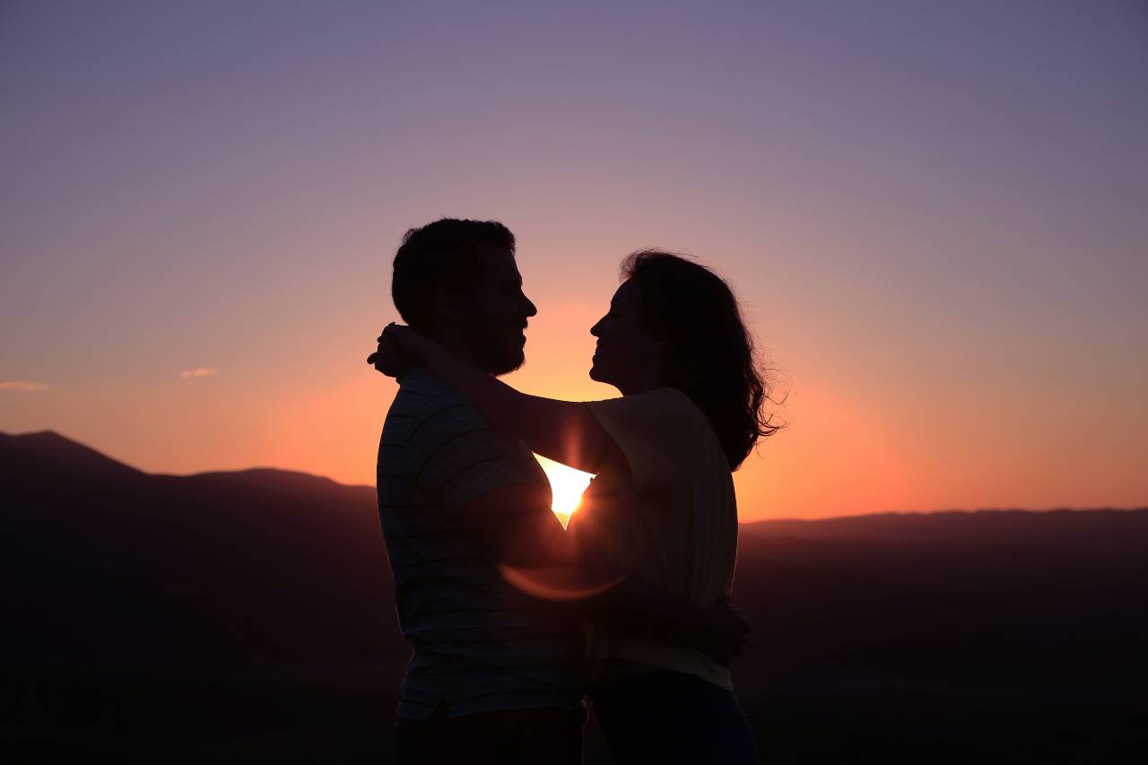 Two people holding each other, silhouetted by the sunset