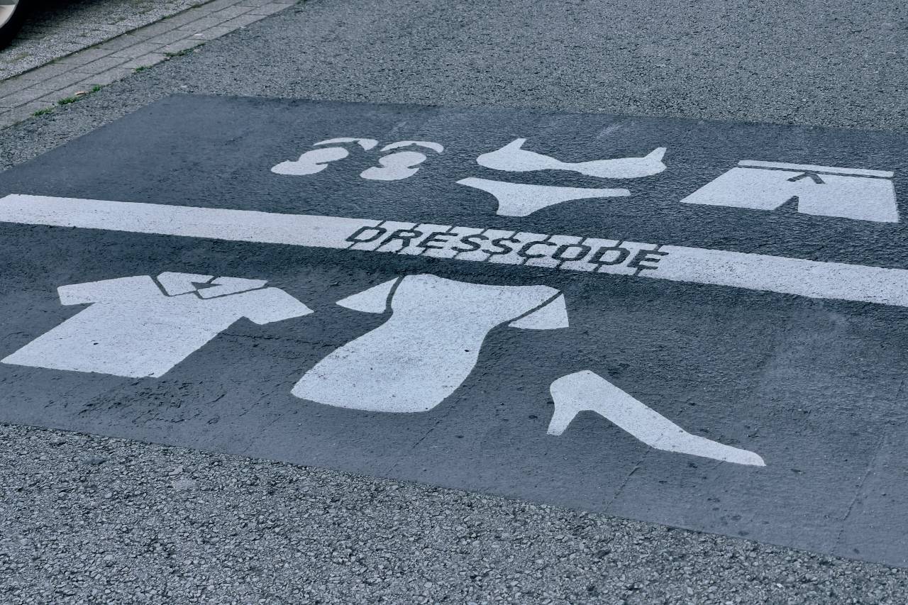 a photo of a painted sidewalk that reads "DRESSCODE" and shows beach clothes on one side and dress clothes on the other