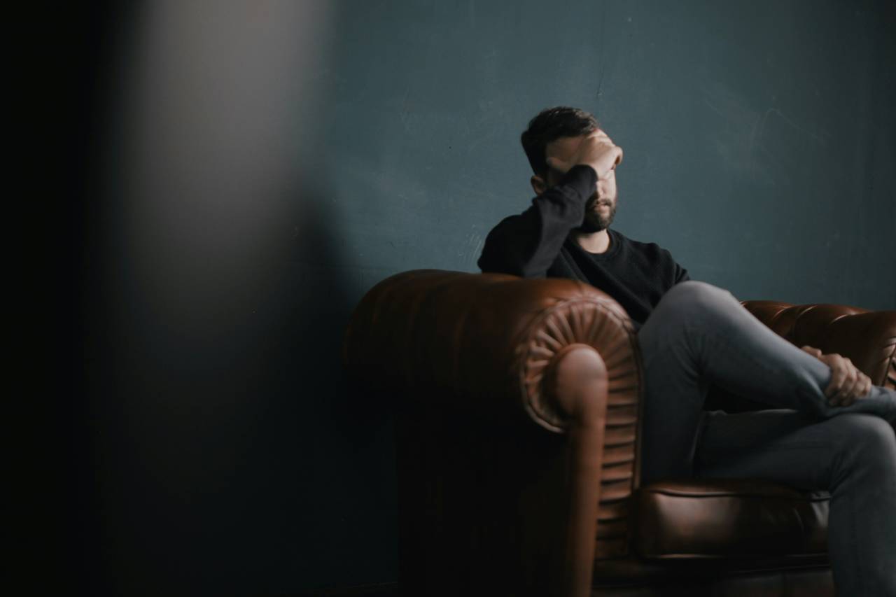 a photo of a man sitting at the end of a couch, hand, over his eyes