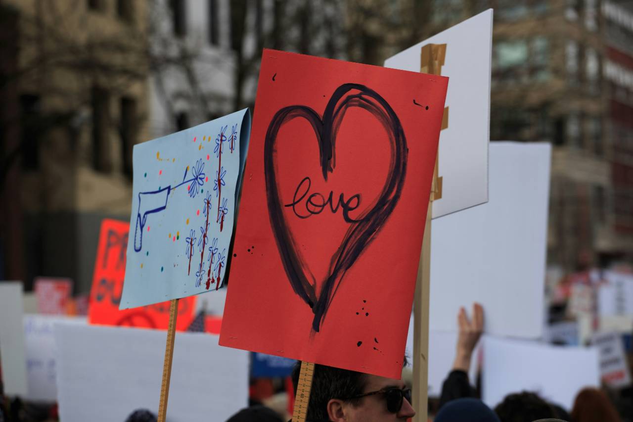 a photo of protest signs, in the middle is a red sign with heart, it reads "love"