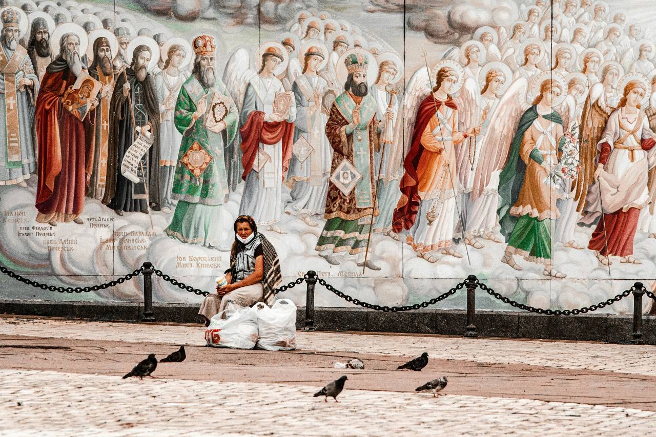 a person sitting on the ground in front of a mural of saints