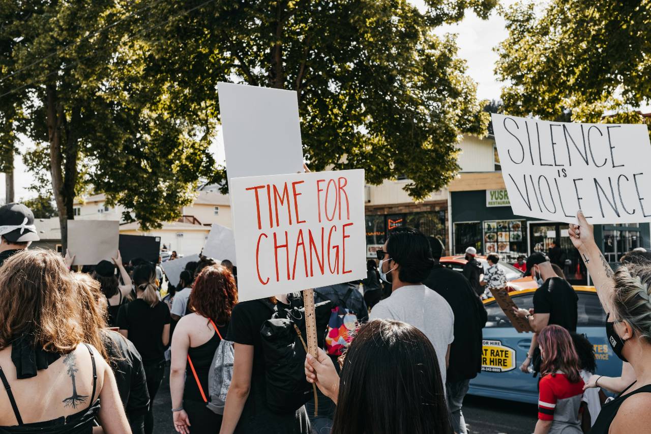 a photo of people marching, with signs that read "TIME FOR CHANGE" and "SILENCE IS VIOLENCE"