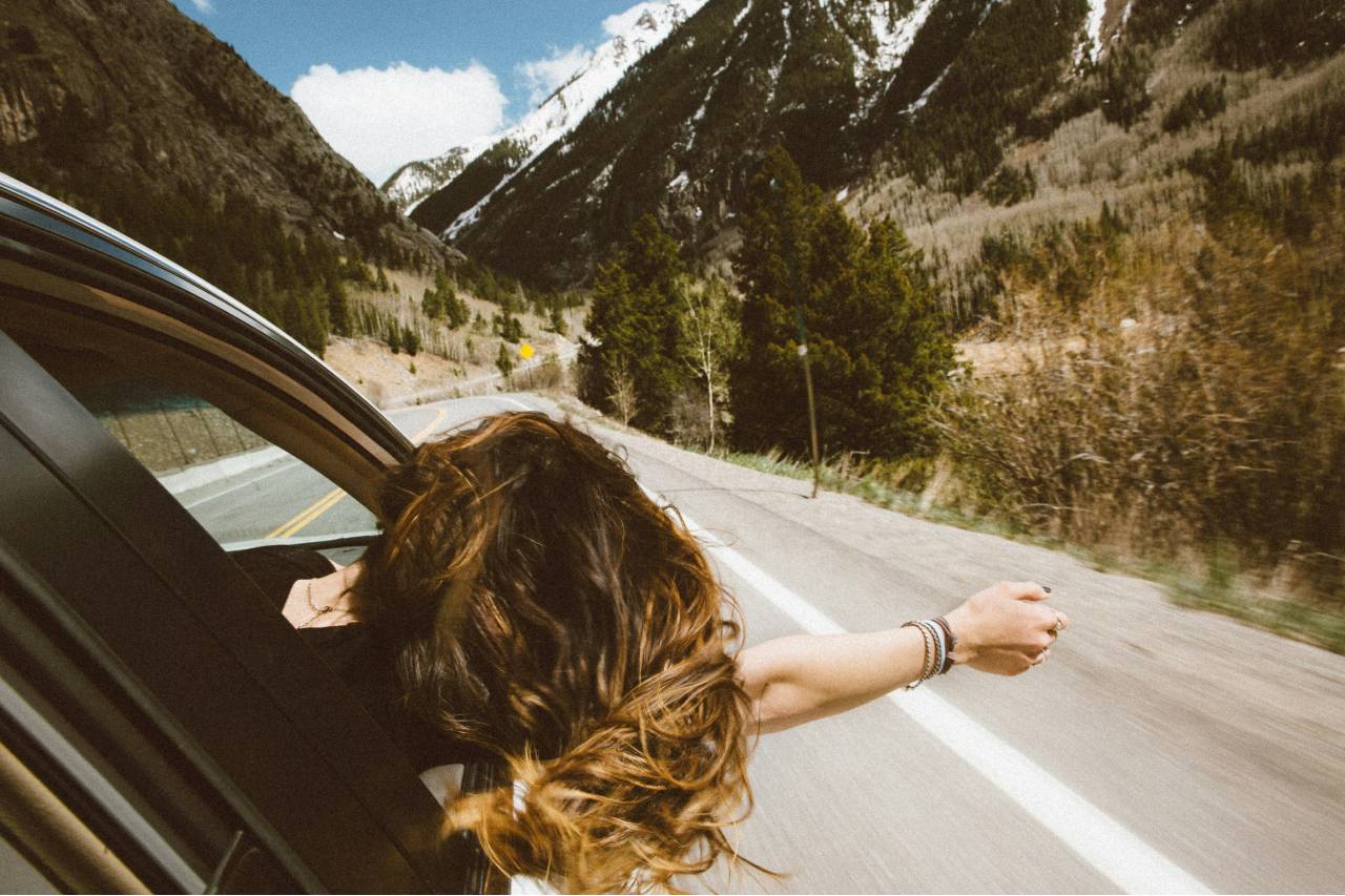 a photo of a person riding in a car, head and hand out the window